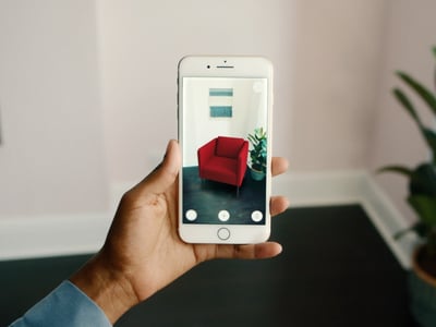Cell phone in foreground shows chair inserted in real-time on image of their living room for AR immersive shopping