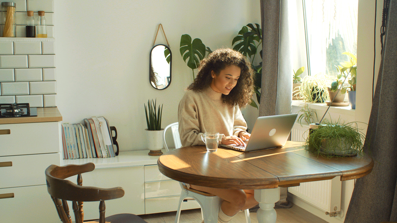 charming young woman typing in kitchen-1045960408